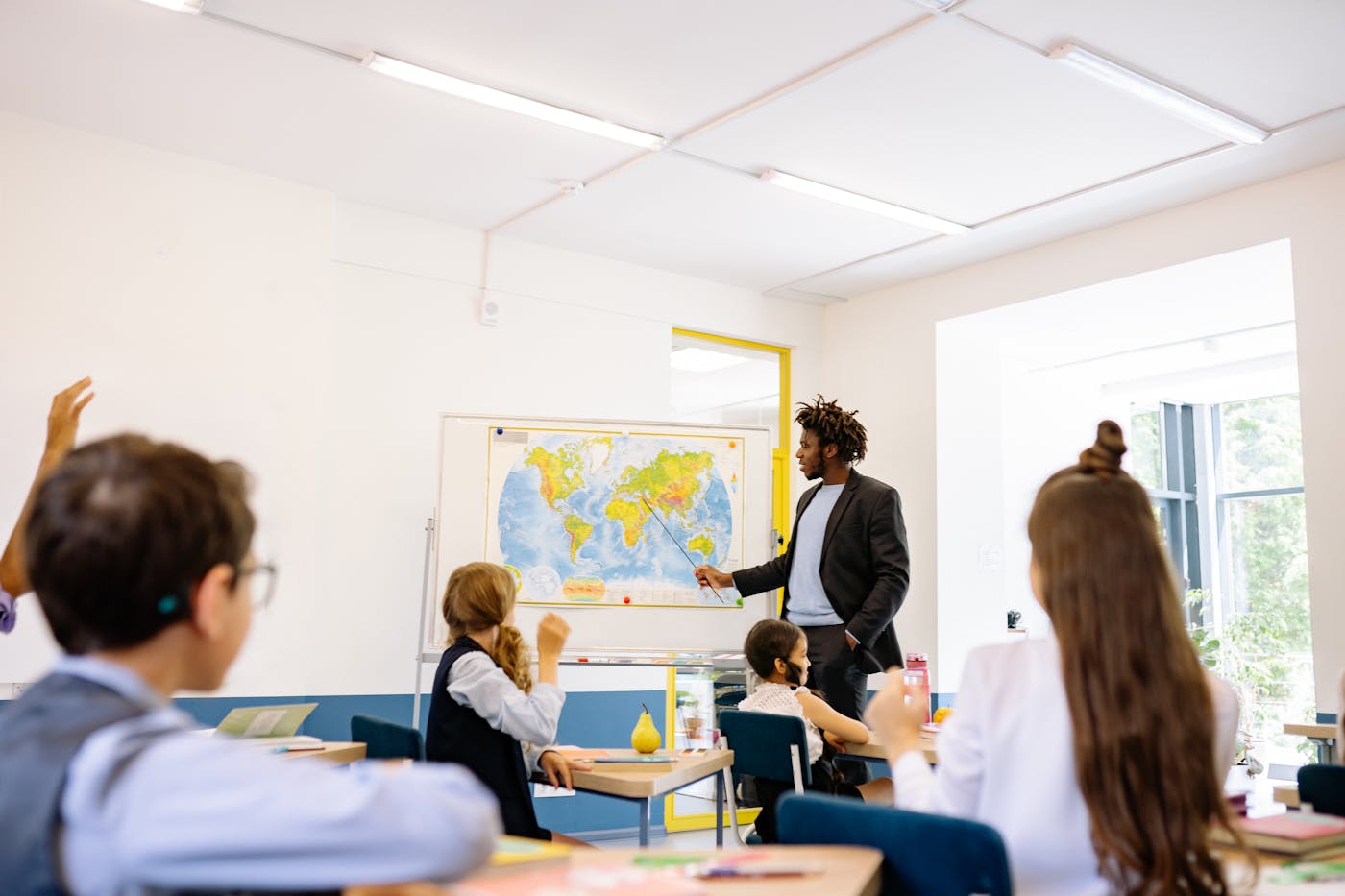 Lehrkraft und Kinder im Klassenzimmer vor einer Weltkarte